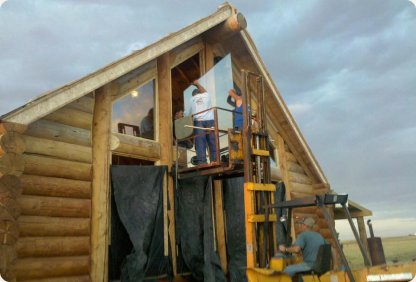 Crew installing large gable windows on a log cabin using a lift