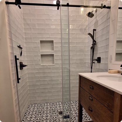 Frameless sliding glass shower door with matte black hardware in a white subway-tile bathroom